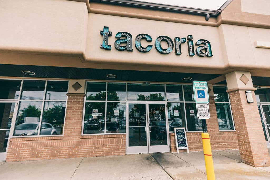 Exterior of restaurant with red brick and signage for "tacoria" 